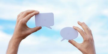 Close-up of hands holding speech bubbles, symbolizing communication and dialogue against a blue sky.