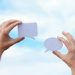 Close-up of hands holding speech bubbles, symbolizing communication and dialogue against a blue sky.