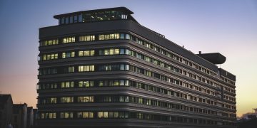 A modern office building beautifully illuminated against the twilight sky in an urban setting.