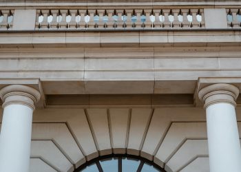 Low angle view of a neoclassical building facade featuring pillars and a balcony in daylight.