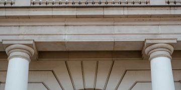 Low angle view of a neoclassical building facade featuring pillars and a balcony in daylight.
