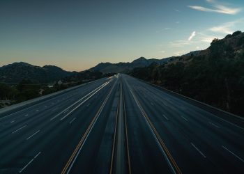 A serene aerial view of an empty mountainous highway at dusk, showing the vastness and tranquility.