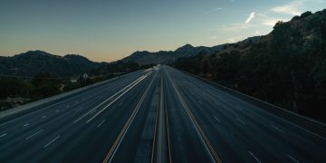 A serene aerial view of an empty mountainous highway at dusk, showing the vastness and tranquility.