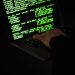 Crop unrecognizable computer geek typing on netbook with codes on screen while hacking system in darkness