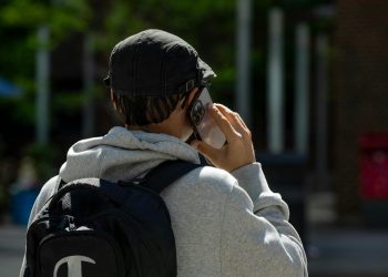 Back view of a man in a cap with a backpack talking on a smartphone outdoors.