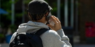 Back view of a man in a cap with a backpack talking on a smartphone outdoors.