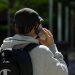 Back view of a man in a cap with a backpack talking on a smartphone outdoors.