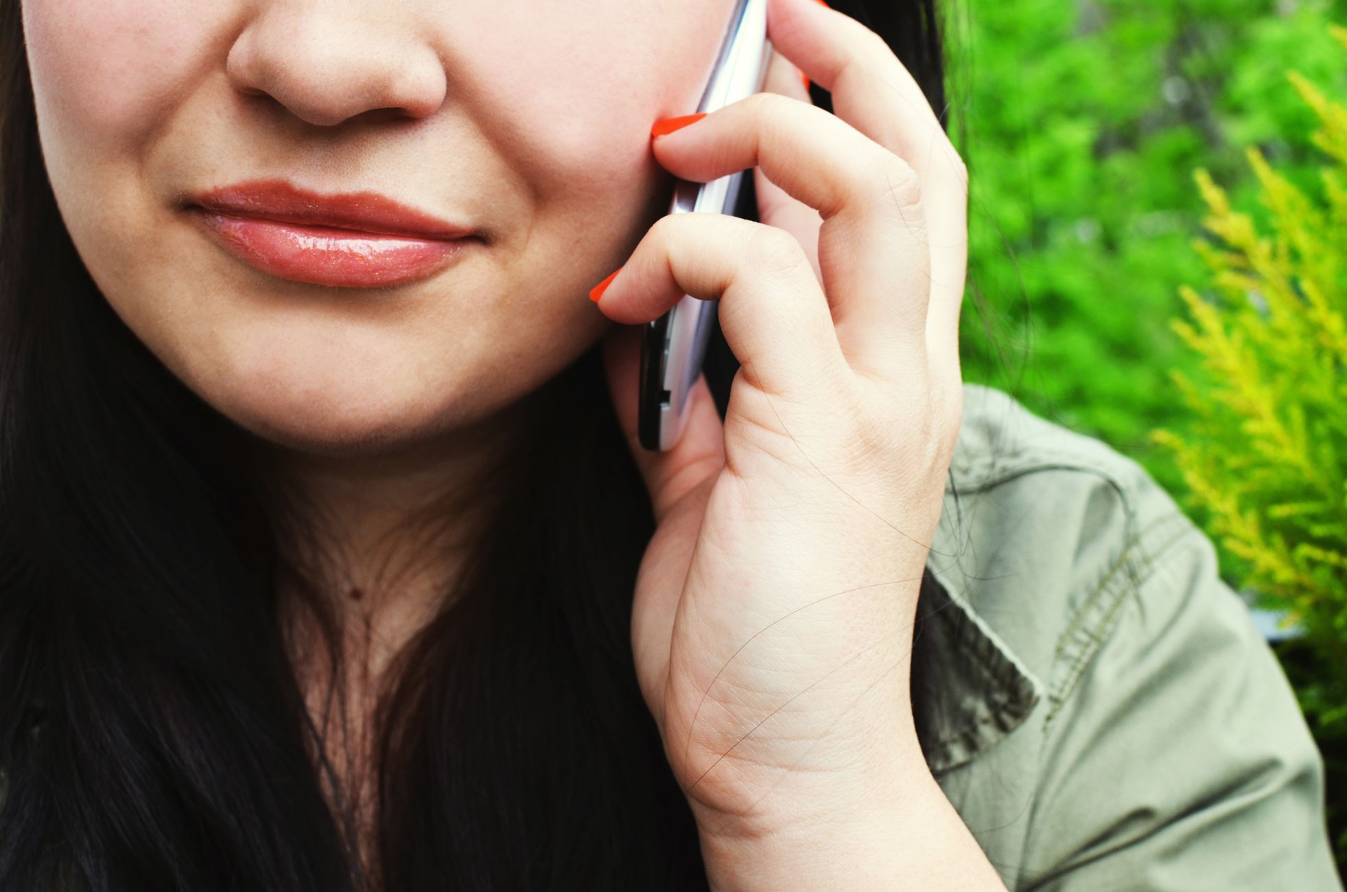 Close-up of a woman chatting on her smartphone outside with greenery in the background.
