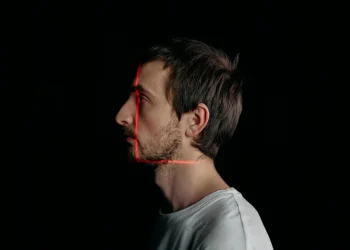 Side profile of a man with red laser scanning lines on his face on a black background.