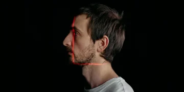 Side profile of a man with red laser scanning lines on his face on a black background.