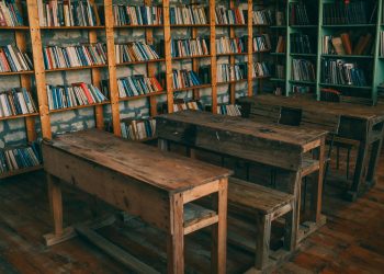 Rustic classroom featuring wooden desks and bookshelves filled with books.