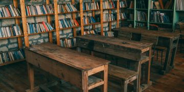 Rustic classroom featuring wooden desks and bookshelves filled with books.