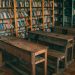 Rustic classroom featuring wooden desks and bookshelves filled with books.