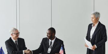 Multinational business meeting with agreement signing, featuring diverse professionals and flags.