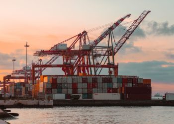 Container cranes at a bustling port during sunset, creating a vibrant industrial scene.