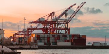 Container cranes at a bustling port during sunset, creating a vibrant industrial scene.