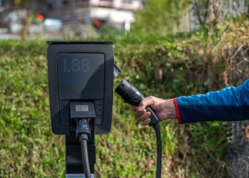 An outdoor electric car charging station with a hand holding a charging cable.