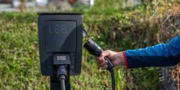 An outdoor electric car charging station with a hand holding a charging cable.