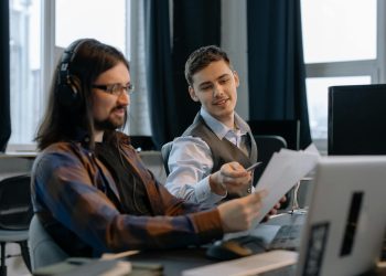 Two colleagues discussing documents at a modern office with computers.