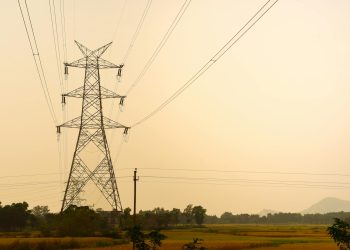 Silhouette of a tall electric tower in a rural landscape during dusk, casting shadows across the fields.