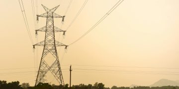 Silhouette of a tall electric tower in a rural landscape during dusk, casting shadows across the fields.