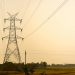 Silhouette of a tall electric tower in a rural landscape during dusk, casting shadows across the fields.