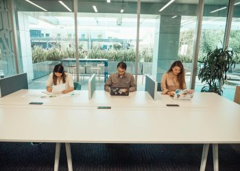 Three professionals collaborating in a modern office space with laptops and documents.