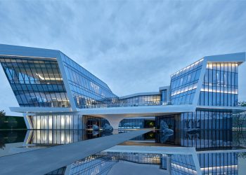 Modern architectural marvel with reflective glass panels by a water body during daytime.