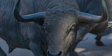 Close-up of a bronze bull statue outdoors, showcasing its powerful horns and detailed craftsmanship.
