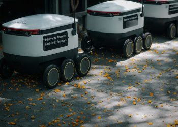 Futuristic delivery robots navigating a leaf-strewn sidewalk, showcasing innovation in modern urban logistics.
