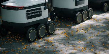 Futuristic delivery robots navigating a leaf-strewn sidewalk, showcasing innovation in modern urban logistics.