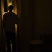 Silhouette of a person standing by a window in a dimly lit room, suggesting themes of solitude and contemplation.