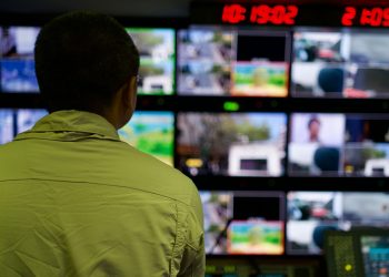 Man in a control room overseeing multiple monitors displaying various scenes.