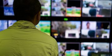 Man in a control room overseeing multiple monitors displaying various scenes.