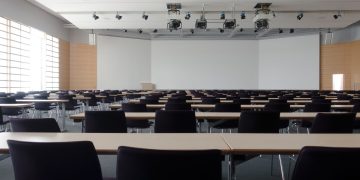 Spacious contemporary conference room with rows of tables and chairs, ready for meetings.