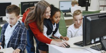 Teacher engaging with diverse children in a technology lesson using computers in a modern classroom.