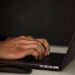 Crop unrecognizable person surfing internet on contemporary netbook and typing on keyboard in dark workspace
