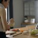 Asian woman preparing a fresh salad with tomatoes and lettuce in a contemporary kitchen setting.