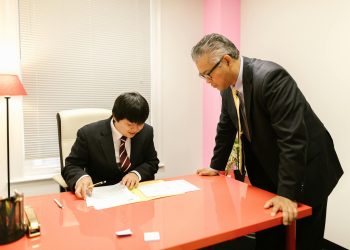 Two businessmen discussing paperwork in a modern office environment.