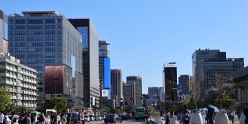 Vibrant street scene in Seoul with skyscrapers and people crossing under a clear blue sky.
