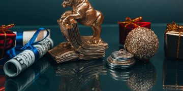 High angle composition of Ox year symbol figurine and wrapped presents placed on mirrored table with coins and rolled and tied dollar banknotes