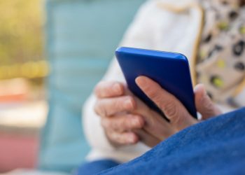 Senior adult using a smartphone outdoors on a sunny day. Focus on hands and device.