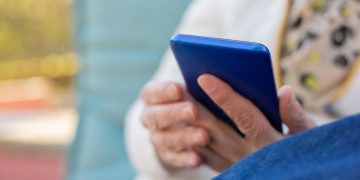 Senior adult using a smartphone outdoors on a sunny day. Focus on hands and device.