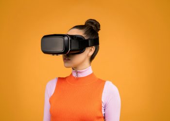 A woman enjoying virtual reality immersion with a VR headset against a vibrant orange background.