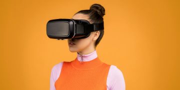 A woman enjoying virtual reality immersion with a VR headset against a vibrant orange background.