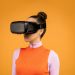 A woman enjoying virtual reality immersion with a VR headset against a vibrant orange background.