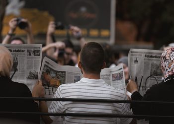 A candid moment of people reading newspapers on a bench in Ankara park.