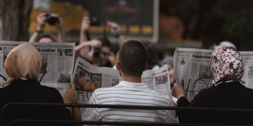 A candid moment of people reading newspapers on a bench in Ankara park.