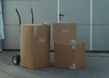 Three cardboard boxes on a dolly, ready for shipping outside a warehouse.