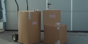 Three cardboard boxes on a dolly, ready for shipping outside a warehouse.
